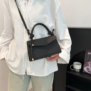 Sac à main noir minimaliste avec texture tressée et poignée nouée porté par un modèle