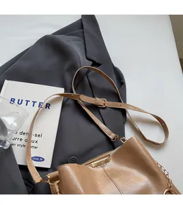 Brown leather bucket bag with adjustable strap placed on a stylish grey blazer background