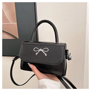 Detail of black glossy handbag featuring silver bow buckle and polished PU leather surface