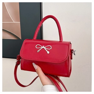 Detail of red patent leather mini bag with silver bow buckle held in hand