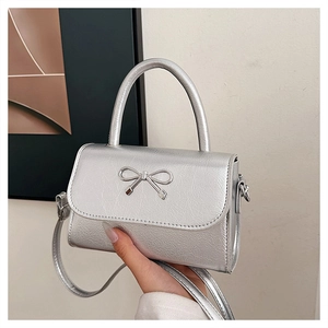 Close-up of silver leather handbag with metallic bow detail and adjustable strap