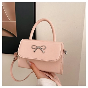 Close-up of small pink crossbody bag with a silver metal bow and elegant leather texture