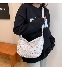 Detail of white quilted crescent bag featuring blue floral bear patterns and wide strap