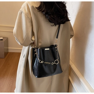 Detail of a black leather bucket bag with gold chain and 'FASHION' hardware on a model