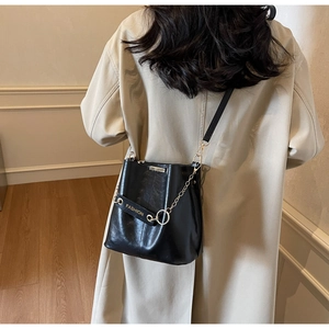 Detail of a black leather bucket bag with gold chain and FASHION embossed strap