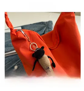 Close-up of orange canvas tote bag with a small plush sheep charm and silver zipper detail
