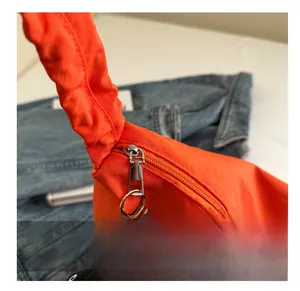 Close-up of a vibrant orange nylon dumpling bag featuring a smooth zipper and silver metal puller
