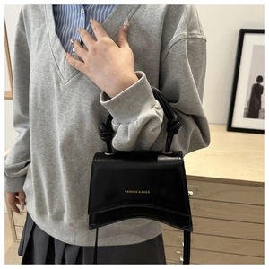 Detail of black matte square bag with gold FASHION & BAGS logo and knotted handle