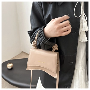 Detail of a beige matte leather handbag with knotted handle and gold lettering