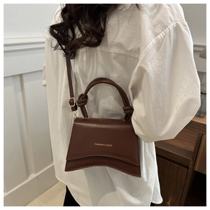 Close-up of dark brown leather handbag with curved base and gold logo lettering