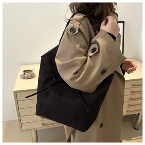 Detail of black suede tote bag with side strap on woman in trench coat at home