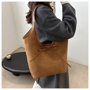 Fashionable dark brown suede tote bag with ribbon bow detail shown on a female model