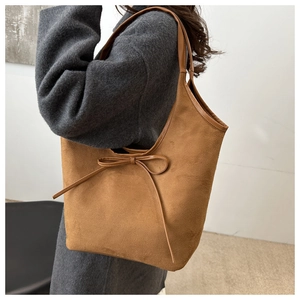 Detail of a brown suede shoulder bag with a bow detail worn over a grey wool coat