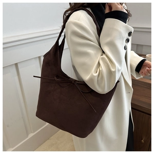 Close-up of a dark brown suede hobo bag with a bow accent worn with a white coat