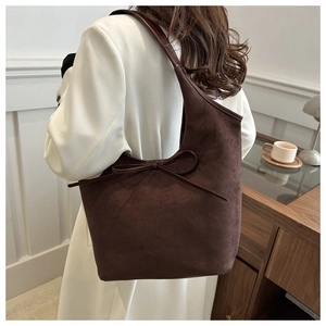 Détail du sac cabas en daim marron foncé avec un nœud décoratif et une texture douce