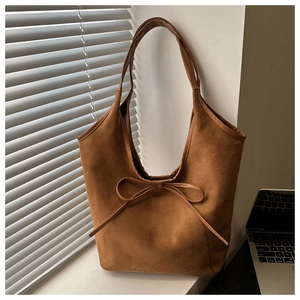 Close-up of brown suede tote bag with delicate bow detail against a laptop and blinds