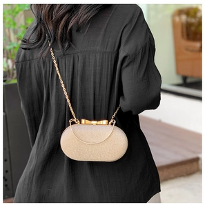 Borsa da sera dorata con chiusura a fiocco e catena indossata su camicia nera