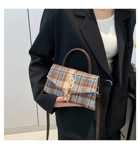 Detalle de bolso bandolera a cuadros con logo S dorado y borla sostenido por modelo