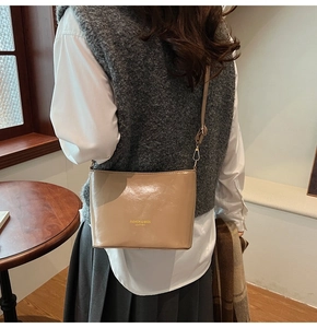 Dettaglio della borsa a secchiello minimalista in pelle kaki con scritte dorate e tracolla