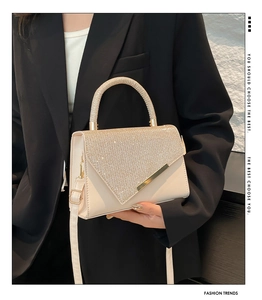 Detail of beige rhinestone underarm bag with gold metal buckle and glossy finish