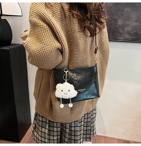 Black glossy leather crossbody bag detail with white fluffy cloud charm on model
