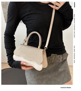 Detail of glitter fabric flap and wavy base on a beige crossbody bag held by a model