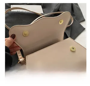 Detailed close-up of the metal magnetic clasp on a cream leather saddle shoulder bag