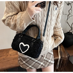 Gros plan d'un sac cylindrique noir en peluche avec détail de cœur et poignée en cuir