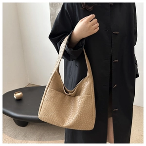 Detail of camel woven tote bag showing texture, worn with a black coat in a minimalist setting
