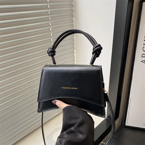 Chic black trapezoid handbag with a unique knotted handle and gold letter print