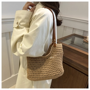 Detailed macro view of hollow hand-woven straw tote bag with brown leather shoulder strap