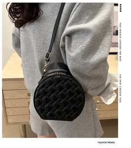 Detailed view of black woven round shoulder bag with golden hardware on a model