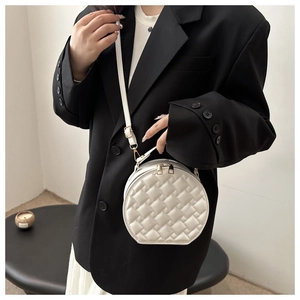Detail of white round quilted crossbody bag with gold zippers and woven texture design