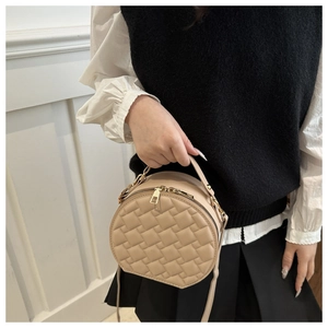 Detail of beige quilted round bag with chain strap and gold hardware on model