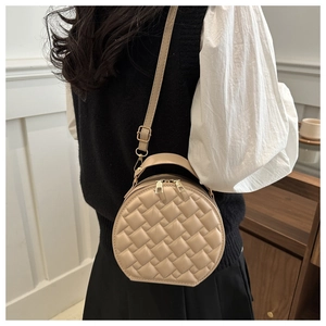 Quilted round crossbody bag in beige PU leather worn by a model in a minimalist room