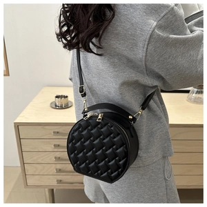Close-up of a black quilted round crossbody bag with gold hardware worn by a model