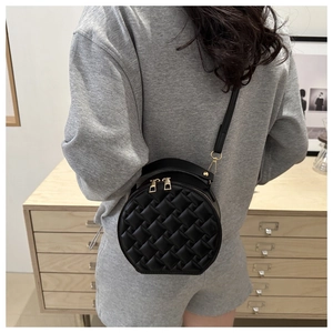 Chic black round crossbody bag with quilted diamond pattern worn by a model in a room