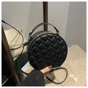 Close-up of a black woven round handbag featuring gold zippers and a circular top handle