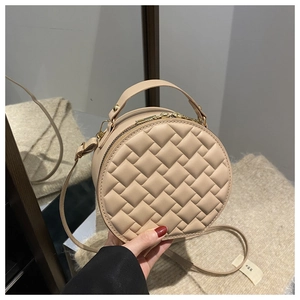 Detail of round beige crossbody bag with quilted texture and gold-tone hardware detail