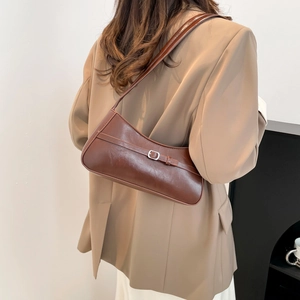 Minimalist dark brown leather shoulder bag with silver buckle worn by a model in office attire