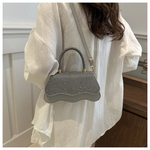 Silver rhinestone handbag featuring unique wavy edge design and circular top handle detail