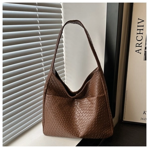 Detail view of large brown woven leather hobo bag with wide strap on a window sill