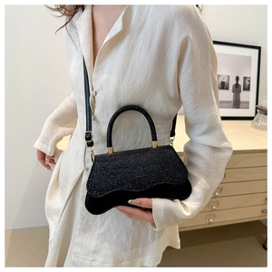 Detail of a black glitter crossbody bag with wavy flap design and gold hardware
