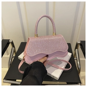 Detail of pink glitter handbag with wavy flap and round handle on a black leather seat