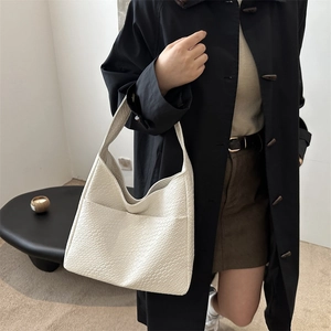 Minimalistische beige Tragetasche mit Krokostruktur und breitem Gurt am Modell