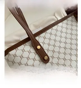 Close-up of white monogram tote bag with brown leather trim and golden metal rivets