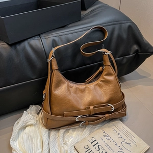 Sac bandoulière vintage marron style motard avec boucles métalliques sur un canapé