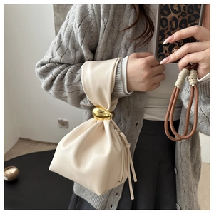 Détail d'un sac seau plissé beige avec une grande poignée en anneau métallique doré poli