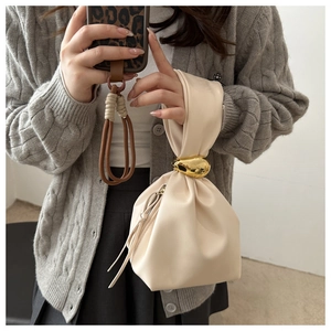 Detail view of cream bucket bag with gold metal buckle and knotted handle on model