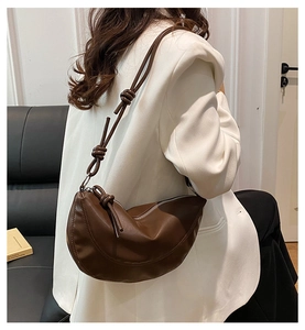 Detail showing brown leather croissant bag with decorative knotted shoulder strap detail
